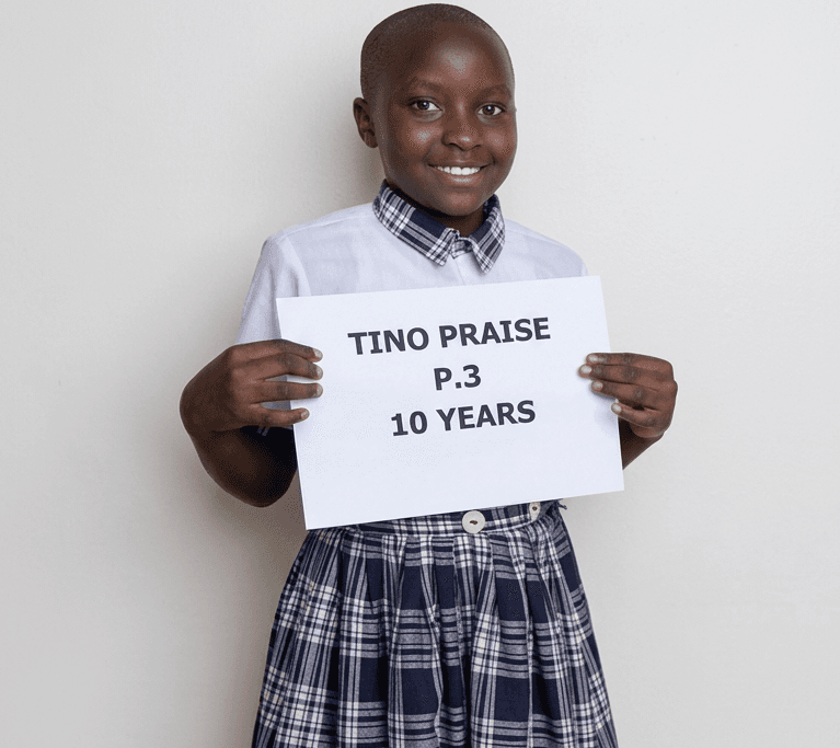 Sponsored student in a school uniform smiling and holding a name sign