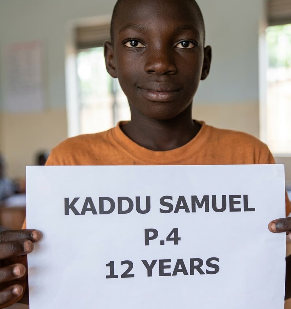 Sponsored student smiling and holding a name sign in a classroom
